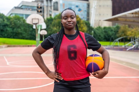 Confident young black woman athlete with braids wearing a red jersey, holding a basketball, and