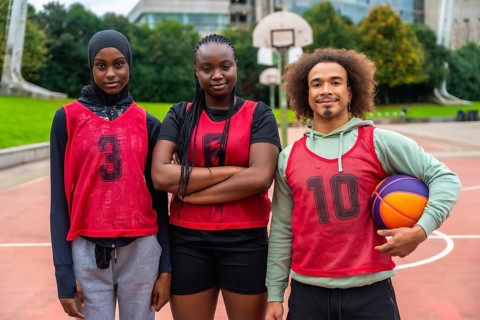 Diverse group of young adult basketball players standing on an outdoor court, proudly wearing