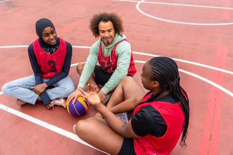 Diverse young friends taking a break on an outdoor basketball court, sitting and talking while