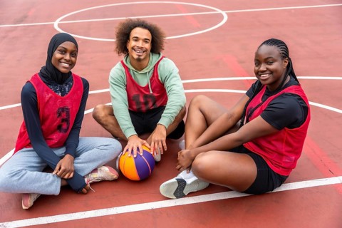 Diverse young friends wearing sport jerseys and a hijab, smiling while sitting together on an