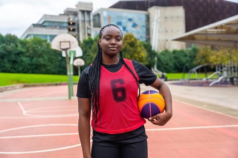 Young black woman wearing a red number six jersey and black athletic attire, standing confidently