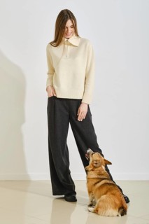 Stylish woman wearing a light sweater and wide-leg pants stands indoors, playfully engaging with a