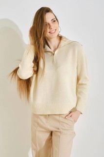 A woman stands in a modern indoor space, smiling with her long hair flowing. She wears a light,