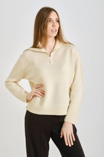 A woman showcases a stylish, cream-colored sweater paired with black trousers in a minimalist