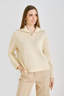 A young woman poses in a trendy cream sweater with a zip collar paired with beige pants. This