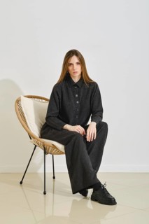 A model sits in a stylish chair, wearing a trendy black shirt and loose pants. Her outfit
