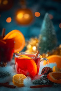 A glass of mulled wine with oranges and cinnamon, golden lights and Christmas decorations in the