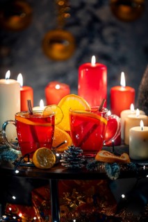Two glasses of mulled wine with cinnamon and oranges in front of red and white candles, Christmas