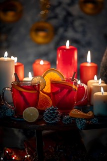 Hot mulled wine with cinnamon sticks and oranges on a Christmassy background with candles