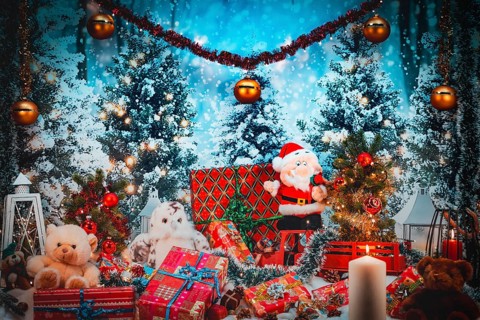 Santa Claus surrounded by gifts, plush toys and festive decorations with a burning candle