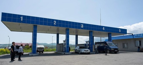 Covered gas station with numbered pillars, several vehicles and people, gas filling station, Sewan,