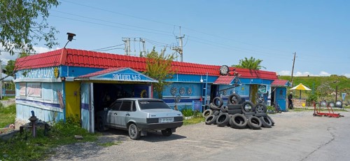 Auto repair shop with stacked tires and vehicles surrounded by rural surroundings under blue skies,