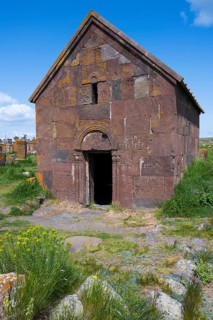 Old Armenian stone church with vaulted entrance surrounded by green landscape, Noratus cemetery,