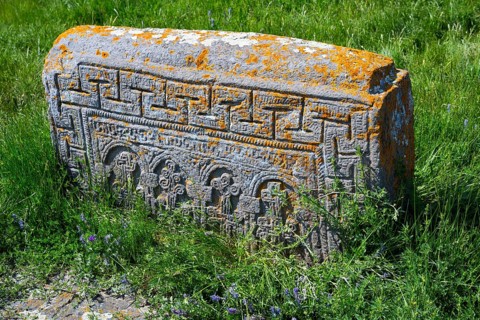 Ancient tombstone set in grass with complex carvings and orange patina, Noratus cemetery, Noradus,