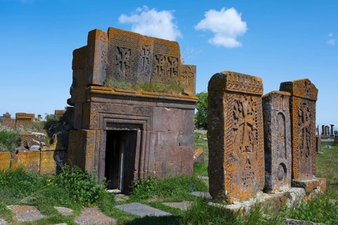 Decorated mausoleum and tombstones with chisels on a green field, crossstones, khachkars, world's