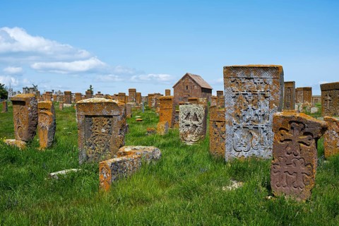 Ancient tombstones with carved patterns on an extensive green meadow, cross stones, khachkars,