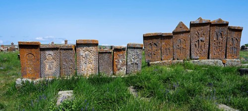 Series of engraved stone monuments on a sunny, green meadow, crossstones, khachkars, world's
