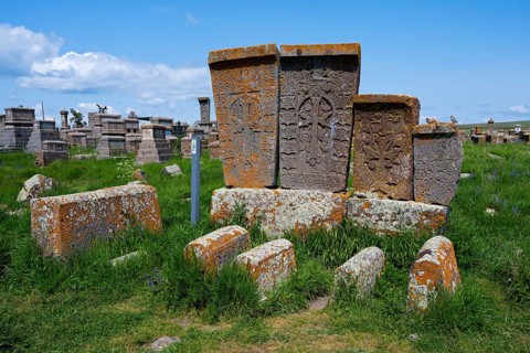 Old tombstones decorated with reliefs on a green meadow under a blue sky, crossstones, khachkars,