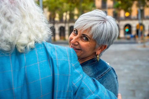 Senior woman with short gray hair smiling over her partner's shoulder as they embrace on a lively