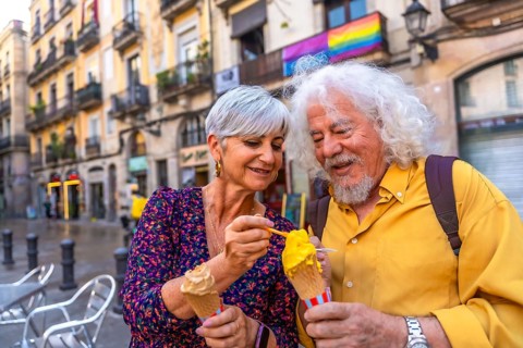 Happy senior couple sharing ice cream while sightseeing in a european city, smiling together with a