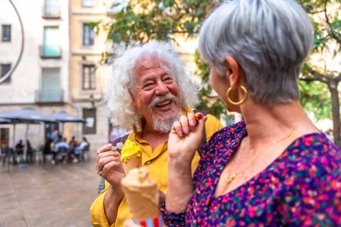 Senior couple laughing and sharing ice cream on a sunny summer date in a lively european city