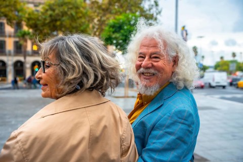 Senior couple walking in an urban environment, the man happily turning and smiling at the camera