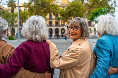 Senior friends walking together in an urban setting, the woman with glasses turning back, smiling