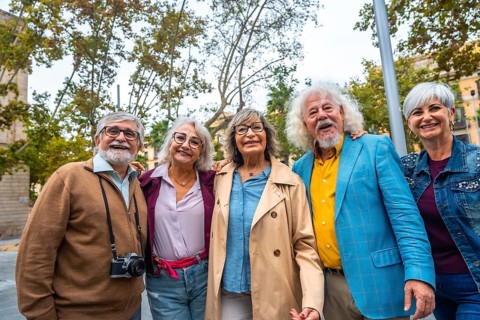 Group of five happy senior friends standing together, smiling and embracing outdoors while