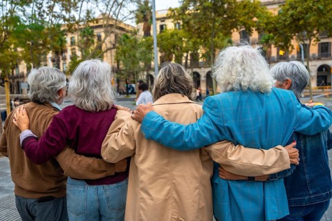 Group of diverse seniors walking together in a city, embracing with arms around each other,