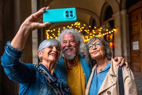 Three happy senior friends enjoying a city trip, smiling and embracing while taking a joyful selfie