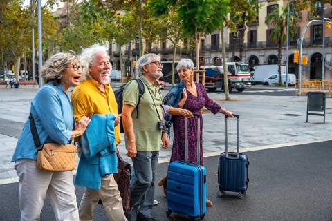 Group of happy senior friends smiling, walking along a city street and pulling luggage, enjoying