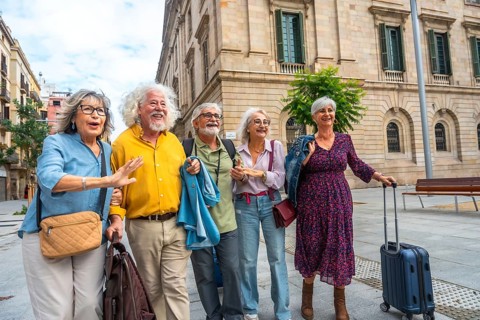 Happy senior friends walking through a sunny european city street with luggage, smiling and