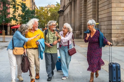 Group of happy senior friends enjoying a joyful trip, walking on a city street, carrying travel