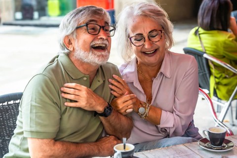 Mature couple laughing and chatting over coffee on a sunny outdoor cafe patio, enjoying relaxed