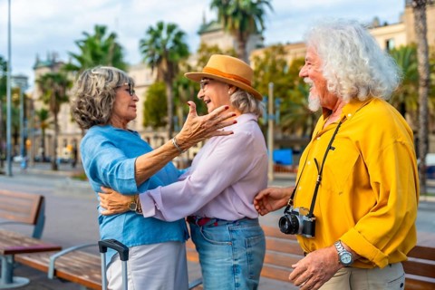 Senior friends embrace in an urban square, joyful reunion while traveling overseas, smiling and