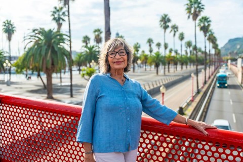 Senior woman standing on a red bridge, smiling directly at the camera, with a vibrant city street