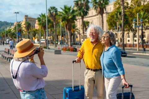Senior friends traveling together, posing for a picture with luggage on a sunny city street,