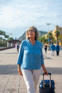 Happy senior woman exploring a city, actively walking with a suitcase, enjoying her vacation and