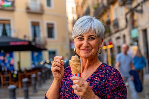 Senior woman smiling while enjoying an ice cream cone on a sunny european city street, relaxed and