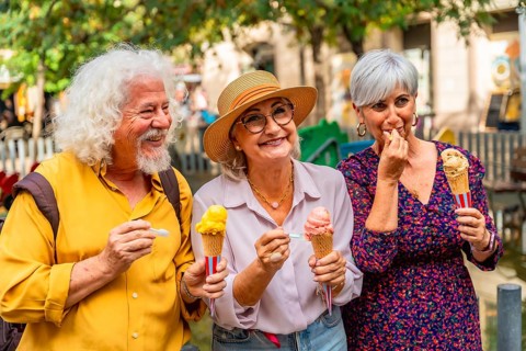 Three happy senior friends, two women and one man, standing outdoors and enjoying colorful ice