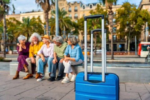 Seniors group relaxing on a bench in a city street with a blue suitcase in the foreground, enjoying