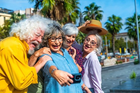 Group of four joyful senior friends laughing and smiling while capturing a memorable selfie with a