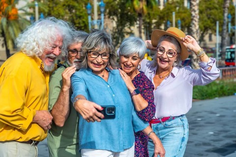 Group of five cheerful seniors enjoying leisure time together, standing close and smiling while