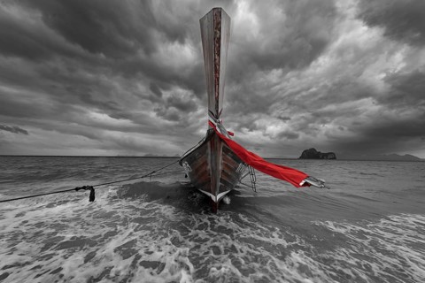 Longtail boat on the beach with dark rain clouds behind it, Koh Ngai island, Andaman Sea, Satun