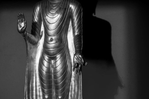 Standing gilded Buddha statue, right hand (raised, open palm outwards) symbolizes the Abhaya mudra,