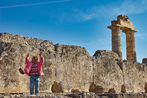 Child standing in front of an ancient column. Stones and sky in the background, Nemea, Ancient Zeus