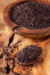 Natural black rice in a wooden bowl and spoon on a wooden surface in rustic style, top view