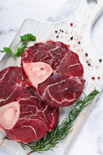 Knuckle on the bone, raw meat for ossobuco, on a wooden chopping board, with a sprig of rosemary,