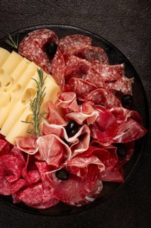 Cold cuts, appetizer, prosciutto, salami and ham, with maasdam cheese and olives, on a round plate,