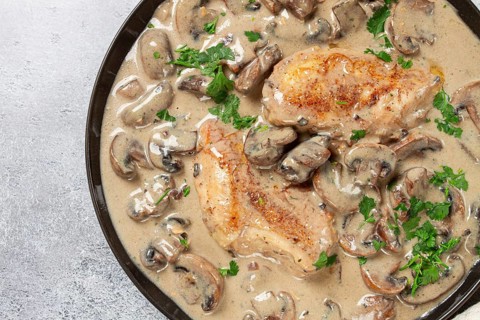 Chicken in cream sauce with mushrooms, on a black plate, no people